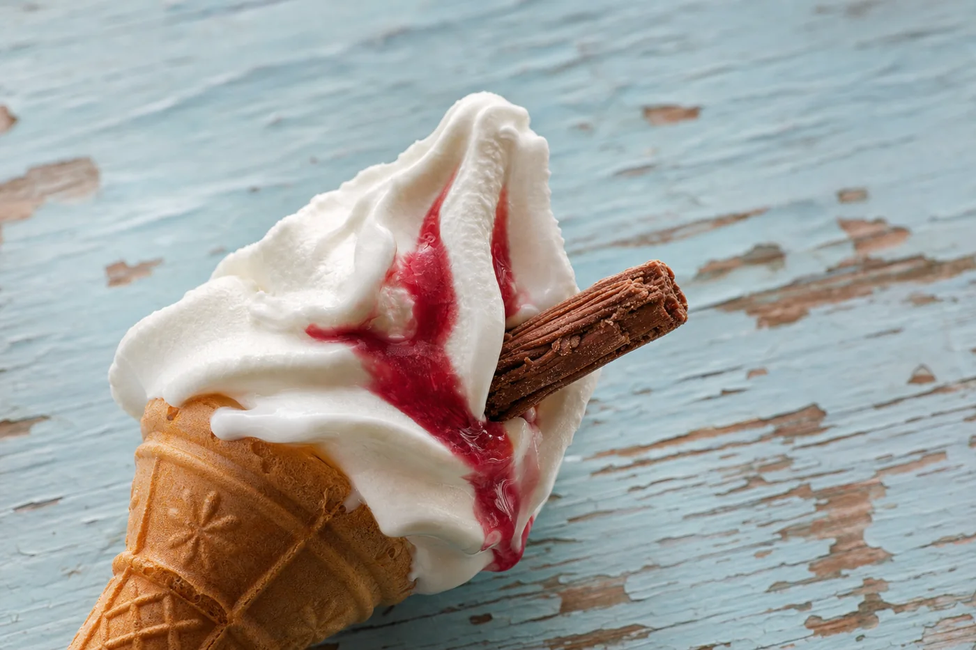 A soft-serve vanilla cone with a chocolate flake on weathered painted wood.