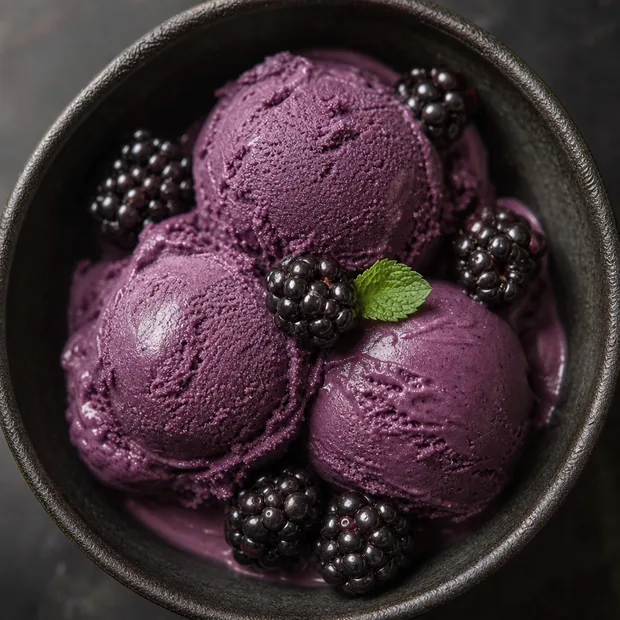 A dark bowl of violet blackberry gelato with fresh blackberries seen from above.